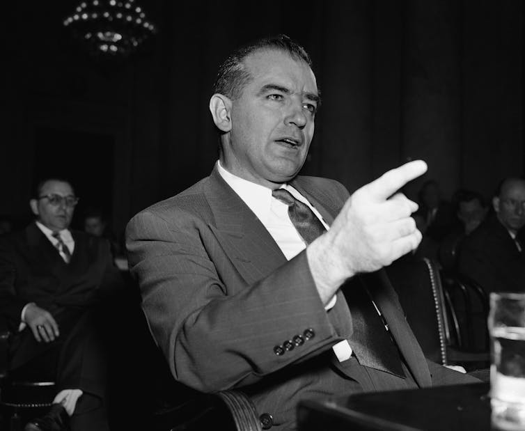 A man dressed in a suit and tie speaks and points his right index finger.
