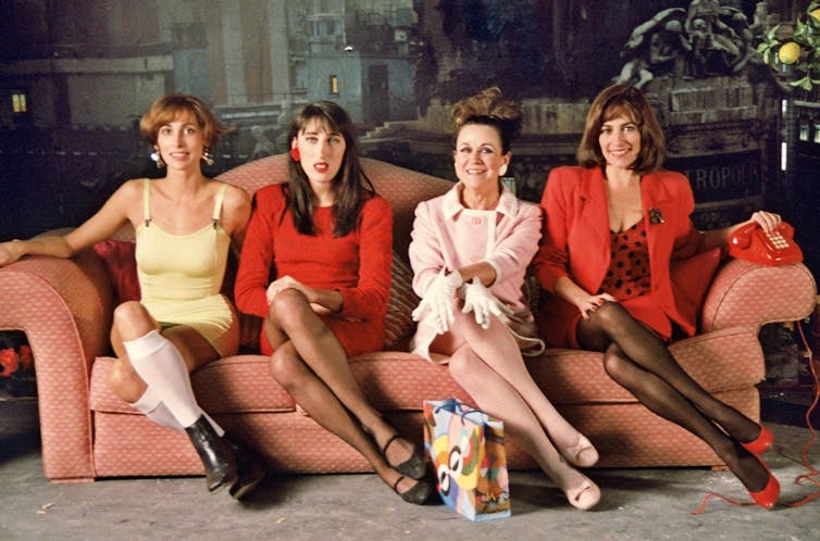 Four women sitting on a sofa with their legs crossed.