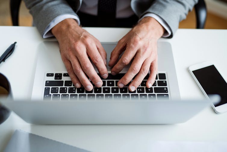 A close-up of hands typing on the keyboard of a laptop.
