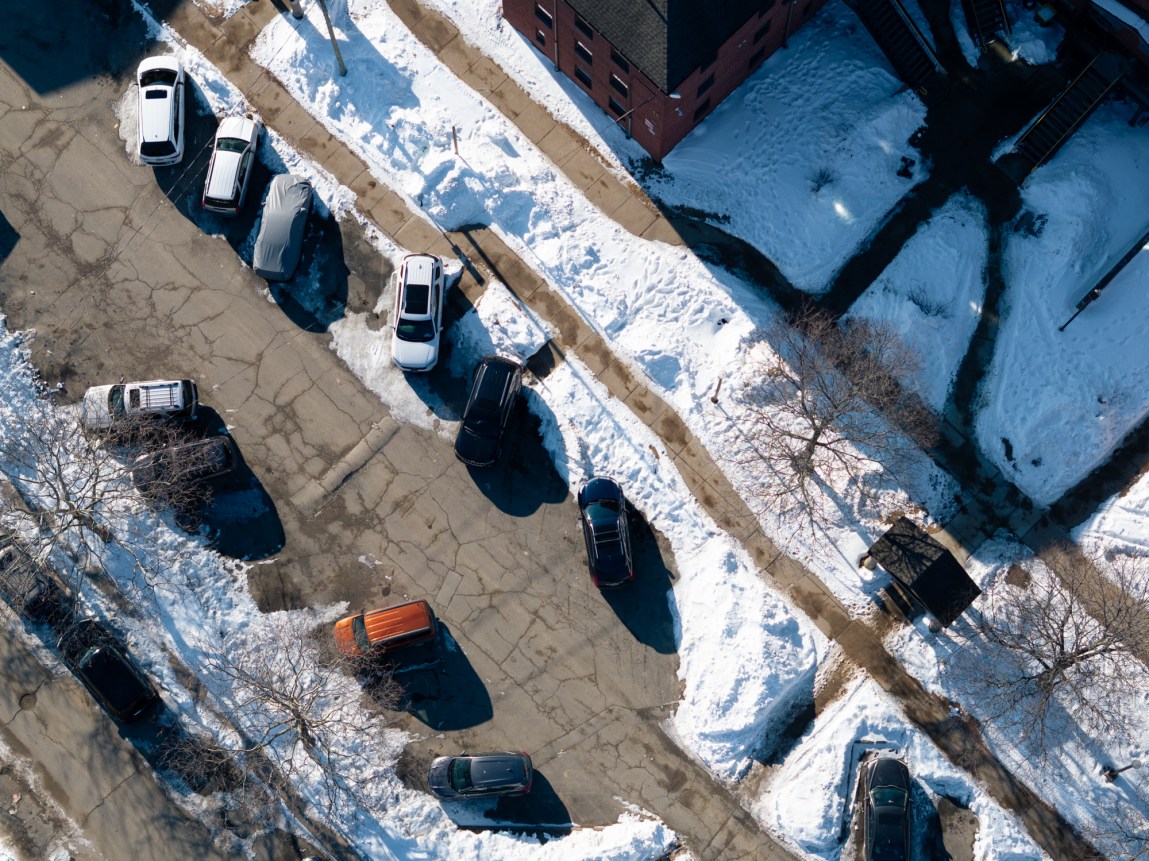 An aerial view of a snow-covered parking lot with some cars parked on snow.