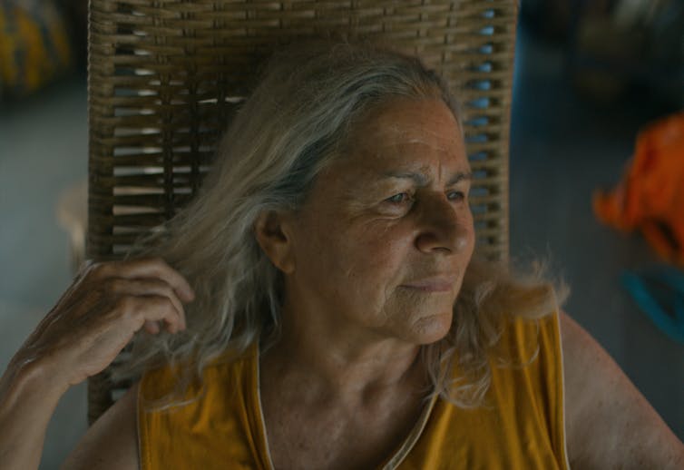 Woman with grey hair in a yellow top, looking content
