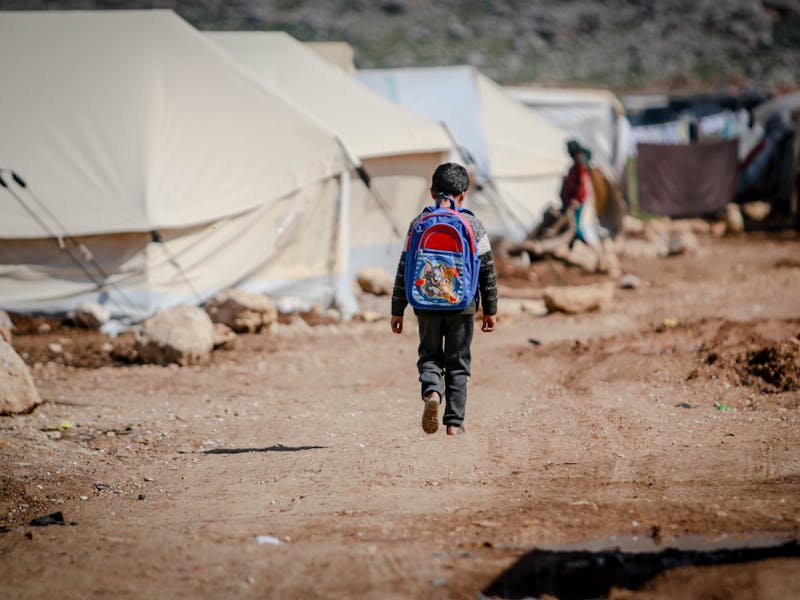 A boy walks along a dirt road at a camp in Idlib, Idlib Governorate, Syria. Photo by Ahmed Akacha on Pexels.