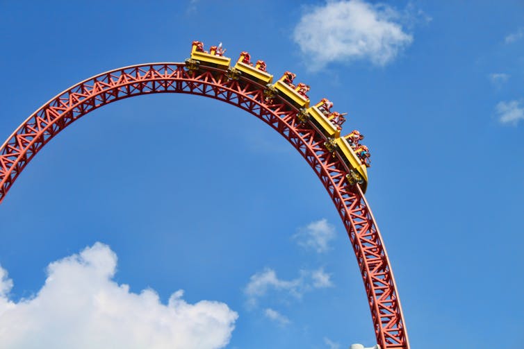 Roller coaster riders at the top of a loop against blue sky