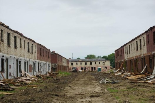 Several large apartment buildings are partially destroyed, with their doors and siding lying in piles in front of them.