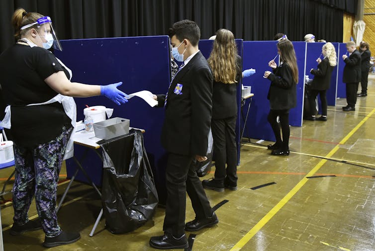 Students in school uniforms seen in small partitioned areas doing COVID tests.