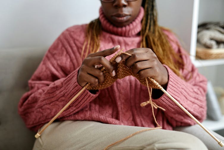 A person in a pink sweater knits while sitting down