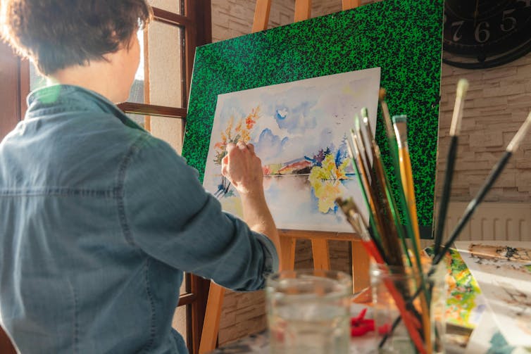 A person paints at an easel with watercolour paint