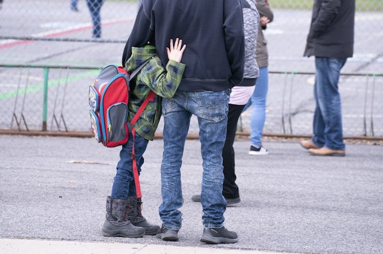 A boy hugging an adult's pant leg.