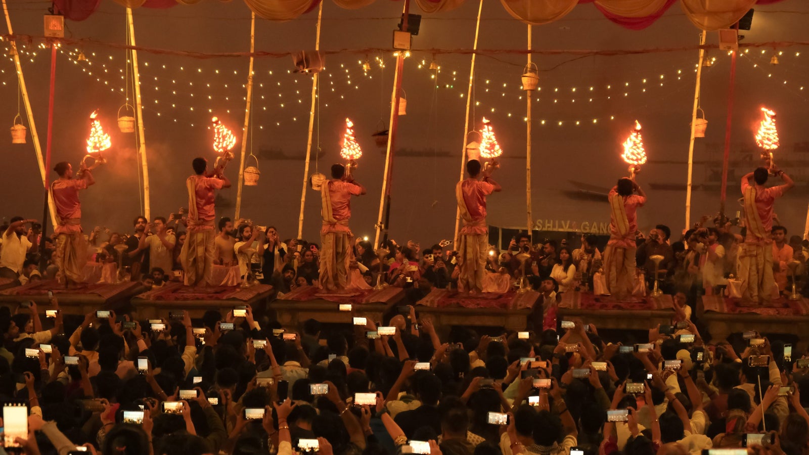 A crowd watches as performers conduct a ritual with flaming torches on elevated platforms during a festive event.