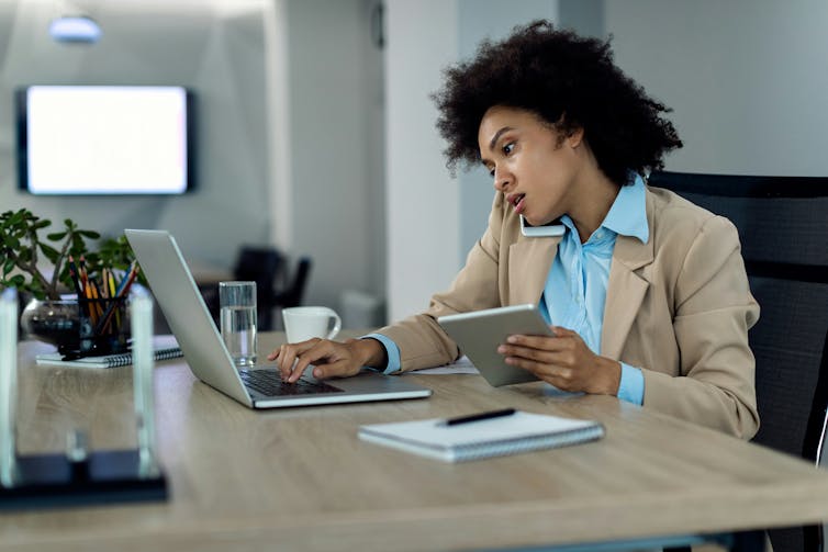 A woman speaking on the phone while typing on a laptop and using a tablet at the same time