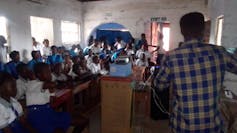 About 40 children in a room watching videos on a projector.