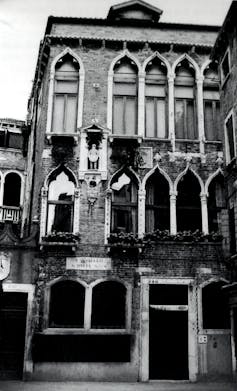 A black-and-white photo of an old, three-story residence with thin, tall windows.