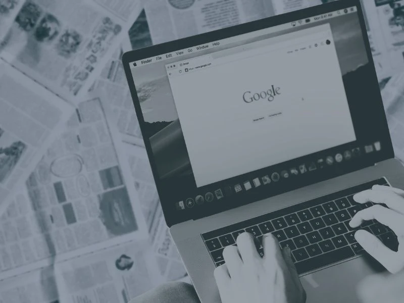 A computer screen open on Google and a background of newspaper pages