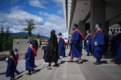 Students in graduation gowns walk down a set of stone steps
