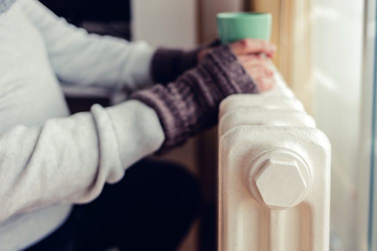 Close up of someone resting their hands and hot drink on a radiator