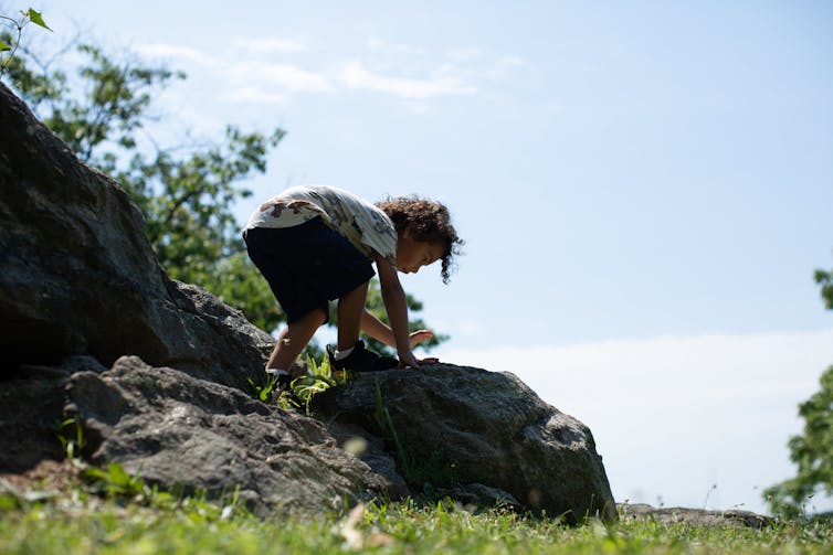 A young child scrambles atop boulders next to grass.