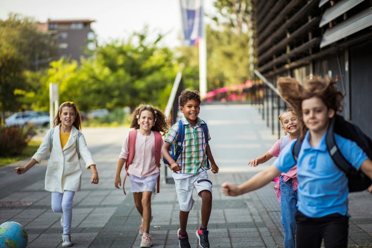 Middle-school age children carrying backpacks smile as they walk down a street.
