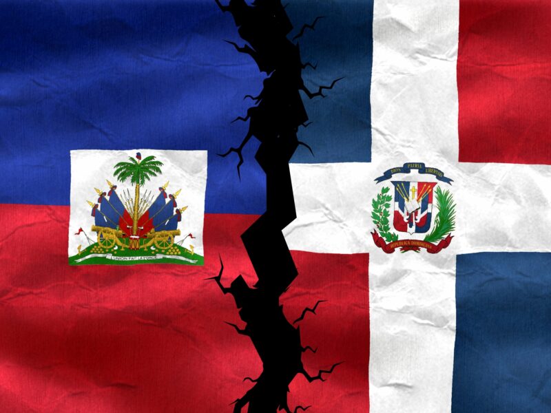 The Haitian and Dominican Republic flags with a fissure down the middle. Feature image created using CanvaPro. 