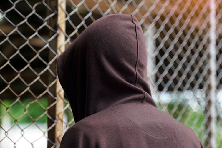 rear view of young person in hoodie facing a chickenwire fence
