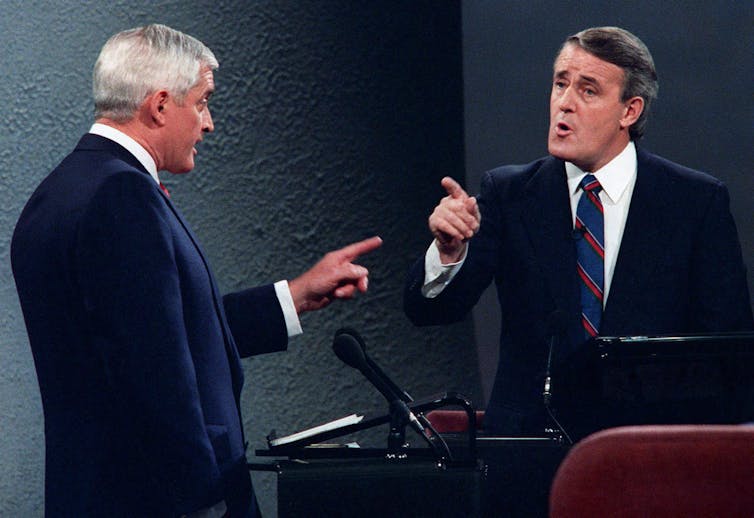 two men, one with white hair, point at each other during a debate