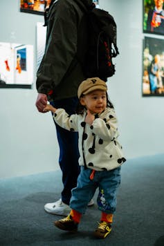 A boy looking very excited holding an adult's hand in a gallery space.