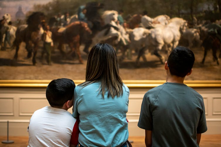 People seen on a bench looking at a painting.