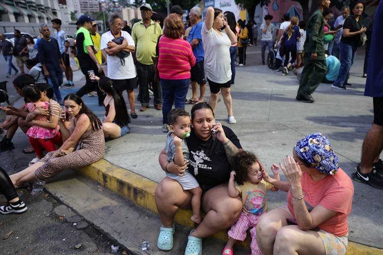 Large numbers of people speak by phone while sitting on curbs and milling around outdoors.