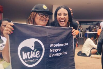Gabriela and Márcia Leite holding up a Black Evangelical Movement flag, at the 2025 Black Women's March in Brasília. 