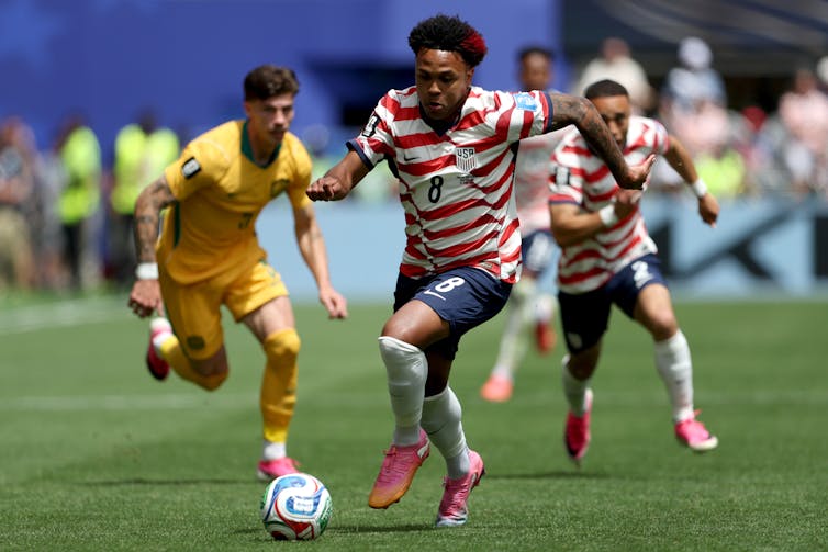 American player chasing down the ball ahead of an Australian player