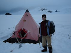 woman in winter gear standing by small red tent in snow
