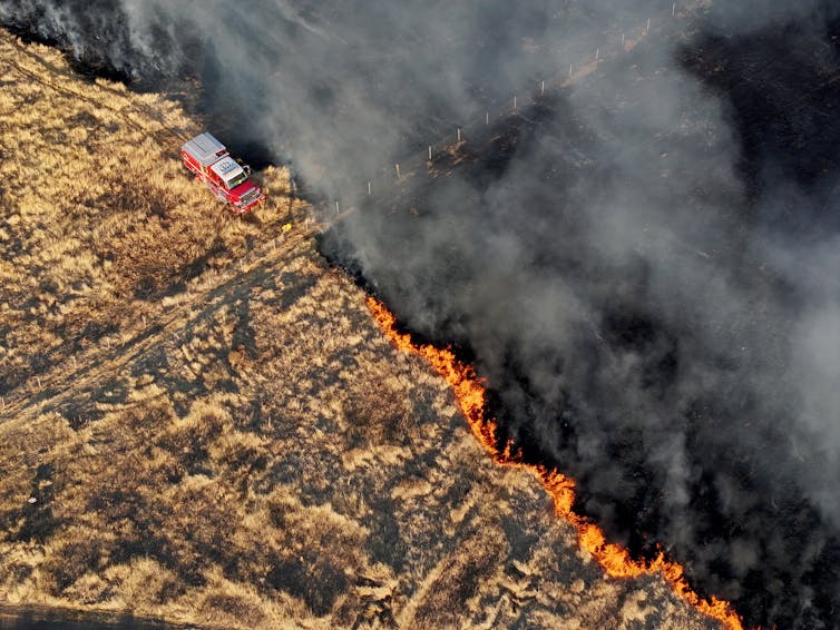 A fire trucks works at the edge of a spreading grass fire