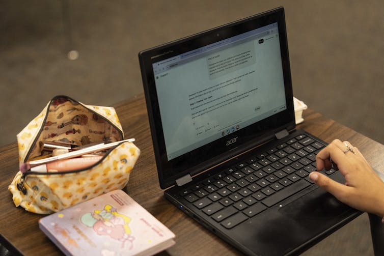 A person's laptop shows a window of ChatGPT and on a table next to this is a pencil case.