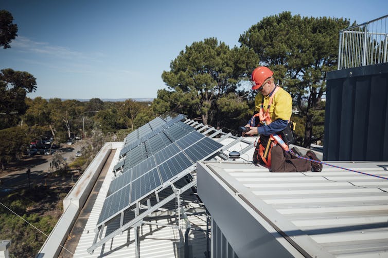 technician installing solar on house in bushy area.