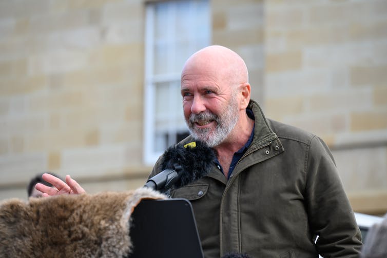 a bald, bearded man behind a microphone