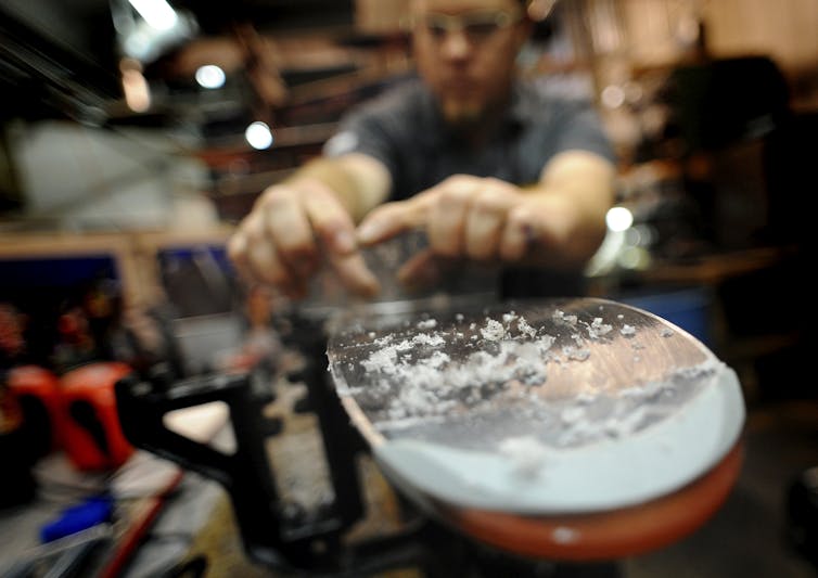 Curls of wax are visible at the end of a ski as a wax technician prepares skis for use.