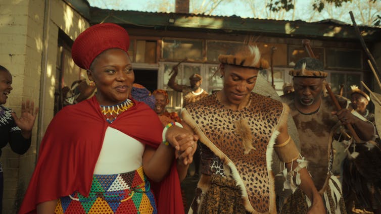 A customary African wedding in traditional attire, a smiling bride and groom walk holding hands.