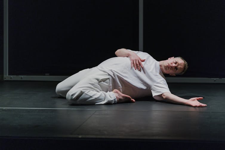 A dancer dressed in white is pictured on the ground mid-dance.