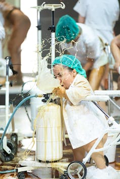 A performer in a white coat pretends to be vomiting onstage.