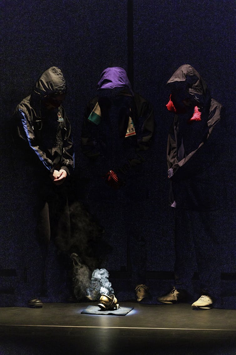 Three hooded figures stand around a smoking thurible.