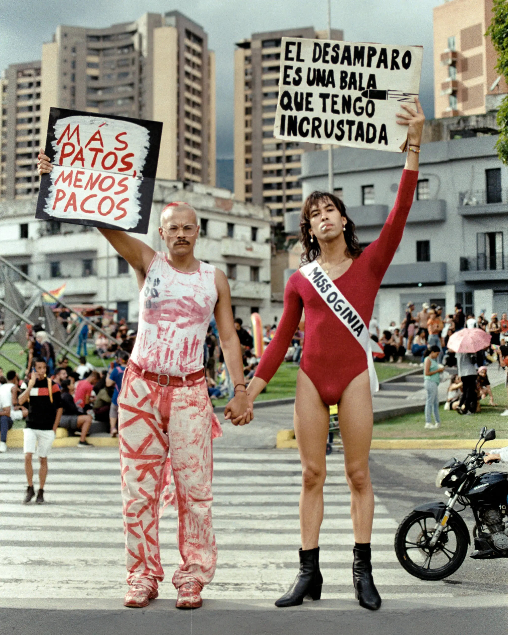 Queer visual artists Yosmel Araujo and Lorenzo Campuzano hold signs during Pride in Caracas, 2024. "More fags, less cops" and "Abandonment is a bullet lodged inside me". Photo by Santiago Méndez. Used with permission. 