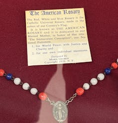 A small explanatory card is positioned next to a string of red, white and blue beads on a chain with a religious medallion.