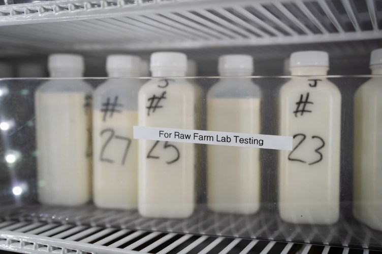 Numbered milk bottles on a refrigerator rack behind tape that reads, “For Raw Farm Lab Testing.”
