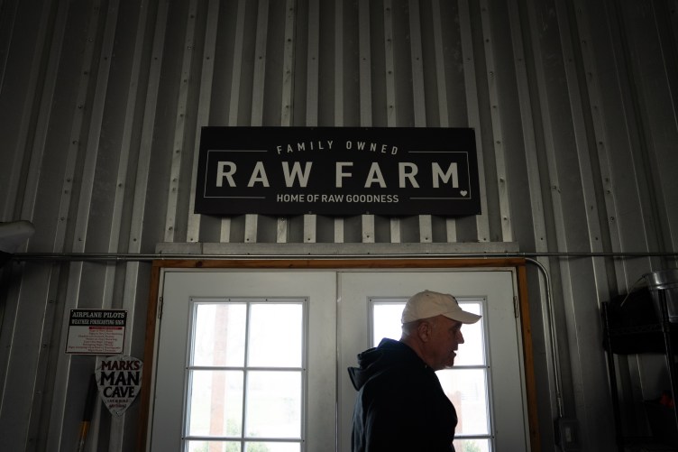 A man in a baseball cap walking out of white double doors beneath a large Raw Farm sign.
