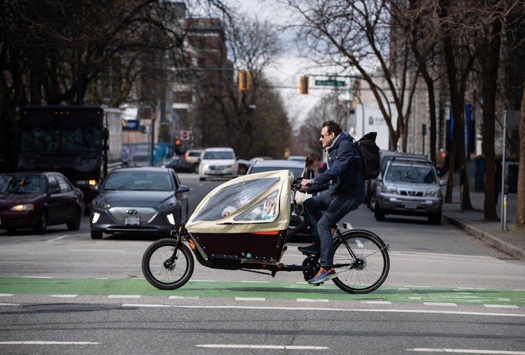 a man rides a bike with a small child and dog in an attached compartment in the front