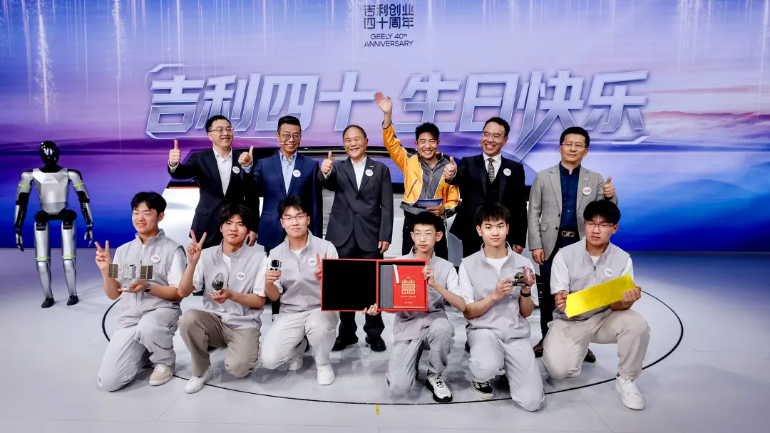 A group of people celebrates Geely's 40th anniversary, posing with awards and a robot in the background