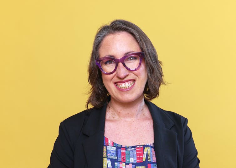a smiling woman wearing a black blazer and dress with bookshelf print