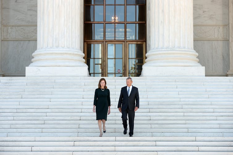 A man and a woman, both in black clothes, walking down a huge set of steps in front of a large building with pillars.