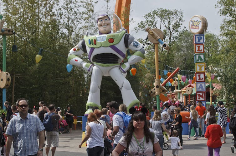Tourists wander through a crowded area under a giant toy astronaut that says 'Toy Story playland'