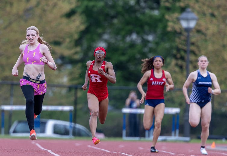 Four young people are seen running close to one another on a track with trees behind them.