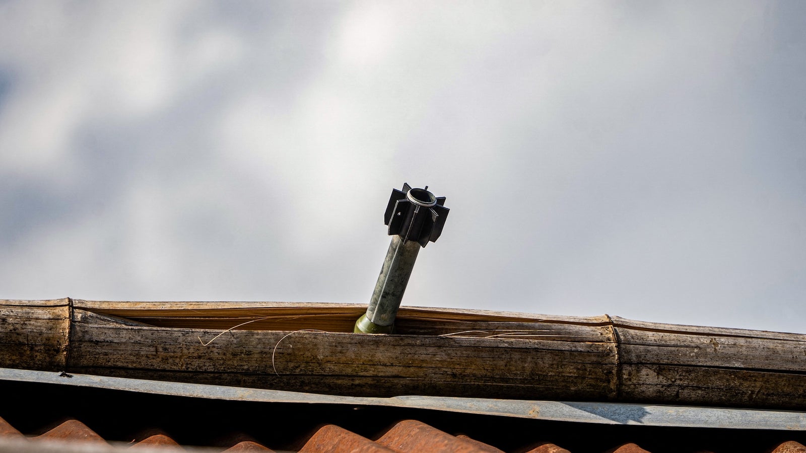 A metal pipe with a black attachment protrudes from a bamboo roof under a cloudy sky